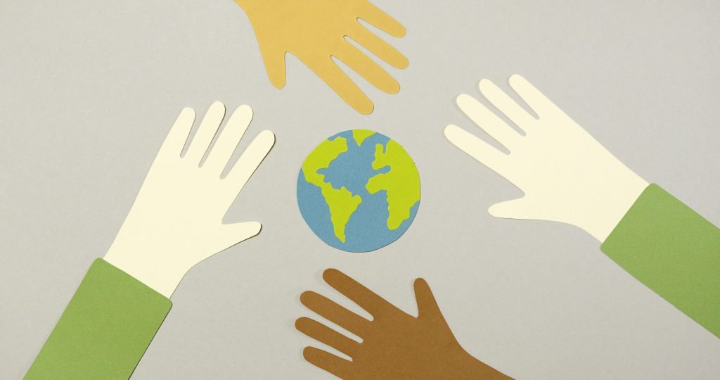 Colorful paper cutouts of diverse hands surrounding a small paper Earth, symbolizing unity.