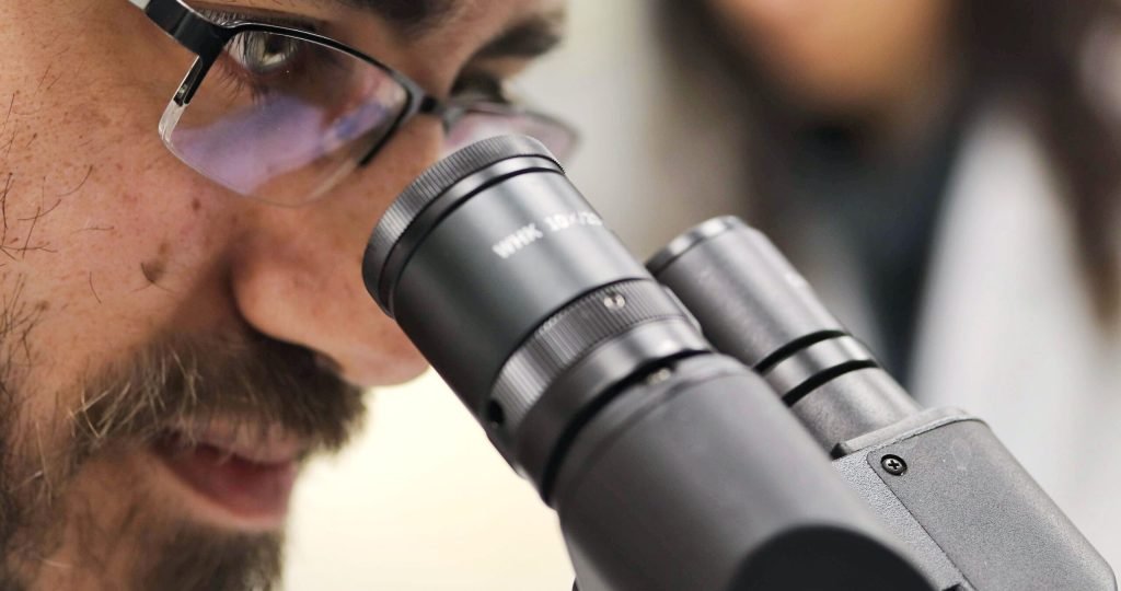 Close-up of a scientist examining samples using a microscope in a laboratory setting.