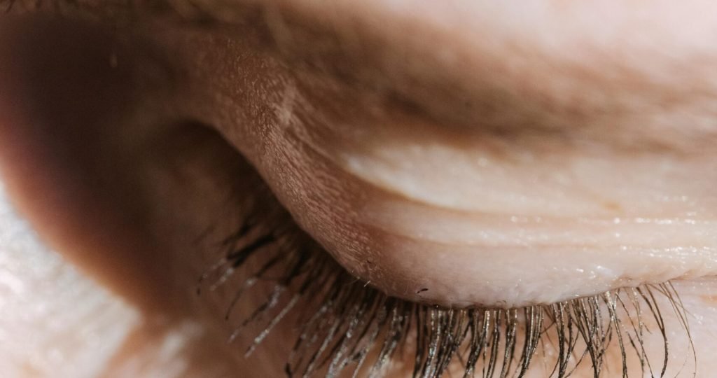 Closeup of crop unrecognizable female with closed eye and long eyelashes with eyebrow standing in light room with sunlight at home