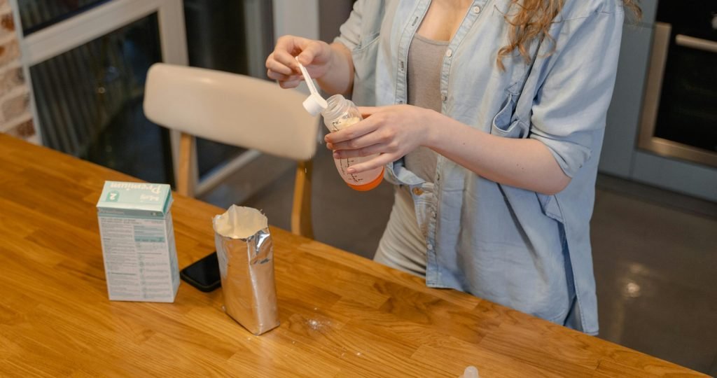 A woman prepares baby formula in a modern kitchen, captured during a daytime routine.