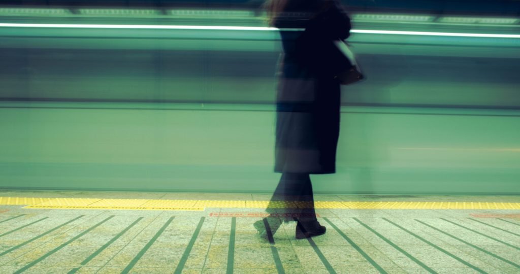 Woman waiting at Istanbul train station, blurred motion capturing a fast-moving train.