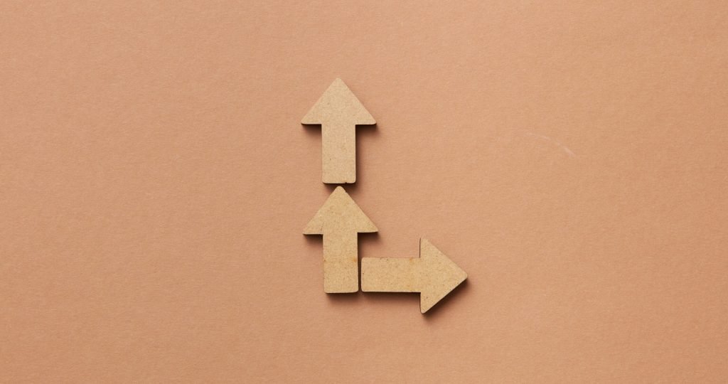 Three cardboard arrows arranged on a brown background, symbolizing direction and choice.