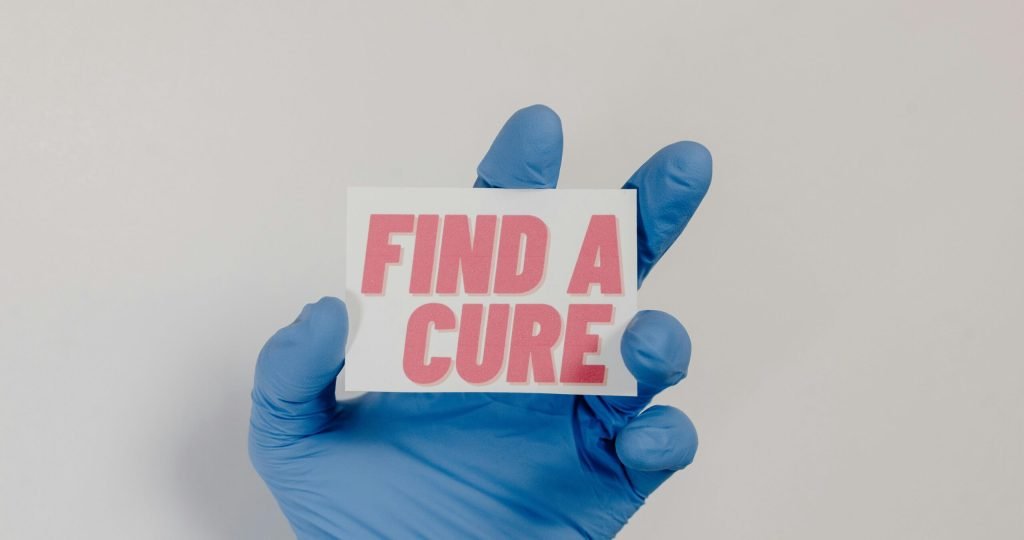 A blue-gloved hand holds a card with 'Find a Cure' message, symbolizing cancer awareness.