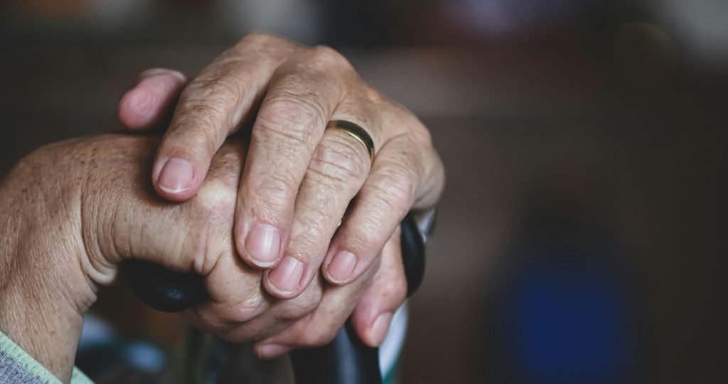 Close-up of senior hands clasped around a cane, highlighting a wedding ring, symbolizing love and support.