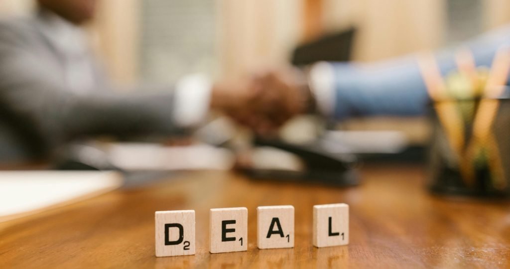 Close-up of Scrabble tiles spelling 'deal' with a handshake in the background.