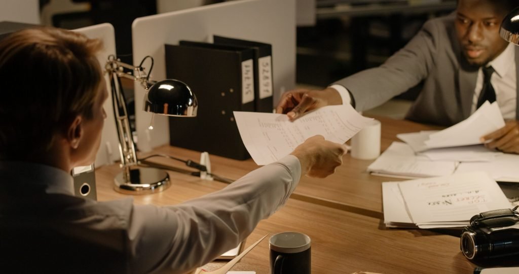 Two business professionals exchanging documents in a collaborative office setting.