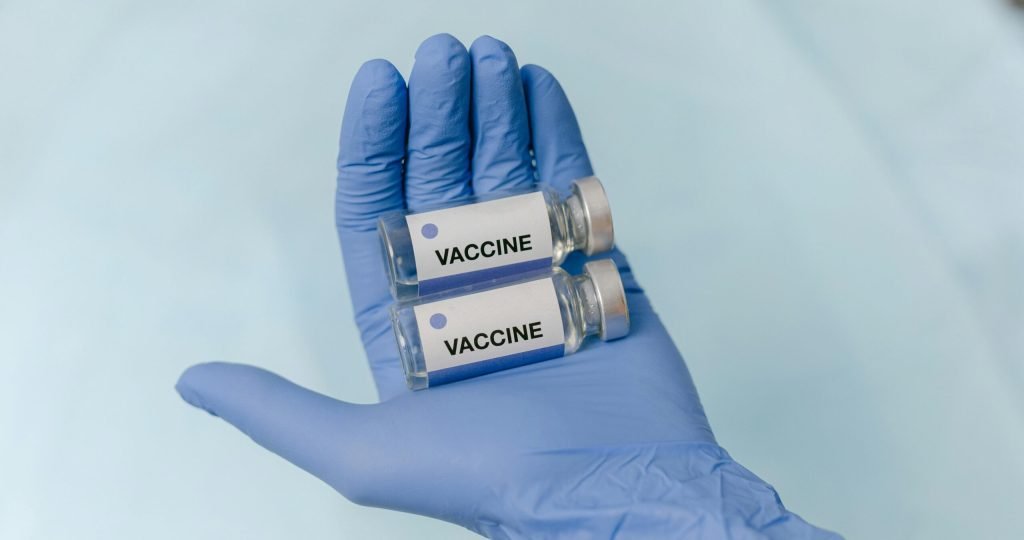 Two vaccine vials held securely in a latex-gloved hand, against a neutral background.