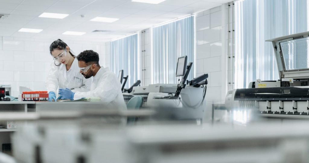 Two scientists working in a high-tech laboratory setting, wearing protective eyewear and gloves.