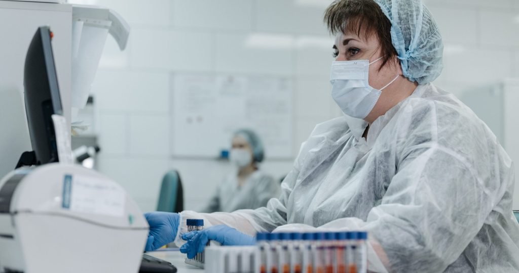 Scientist in protective gear working with lab equipment and samples in a laboratory setting.