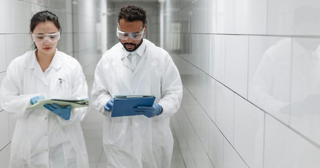 Two researchers in lab coats review documents in a clinical laboratory hallway.