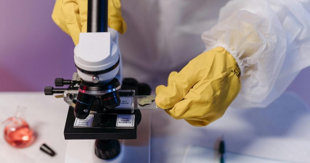 Researcher in protective gloves examines samples under a microscope in a lab setting.