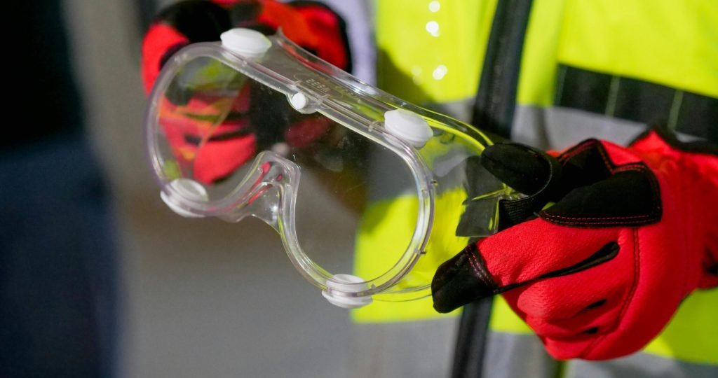 Close-up of a person holding safety goggles with protective gloves, featuring high visibility gear.
