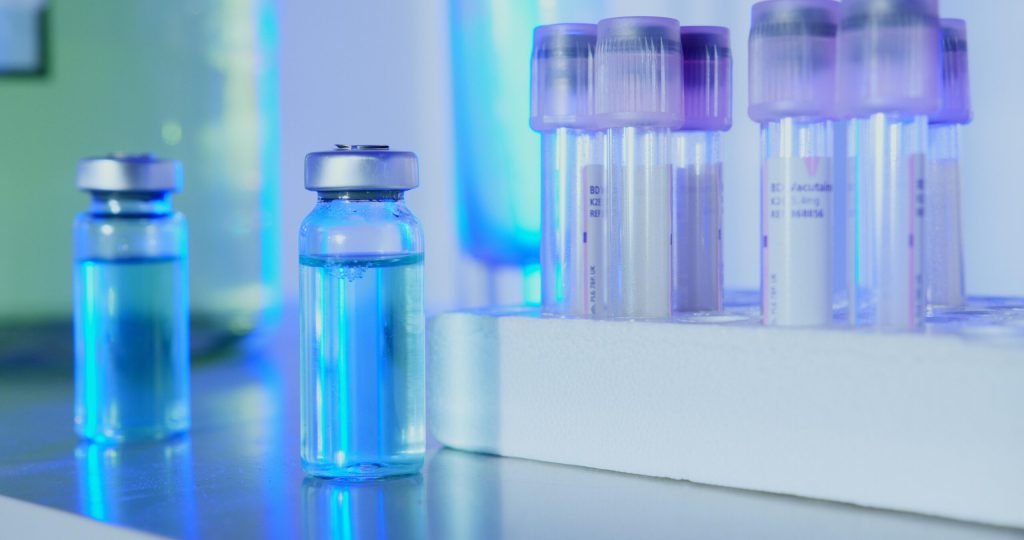 Vials and test tubes with blue liquid in a laboratory setting under fluorescent light.