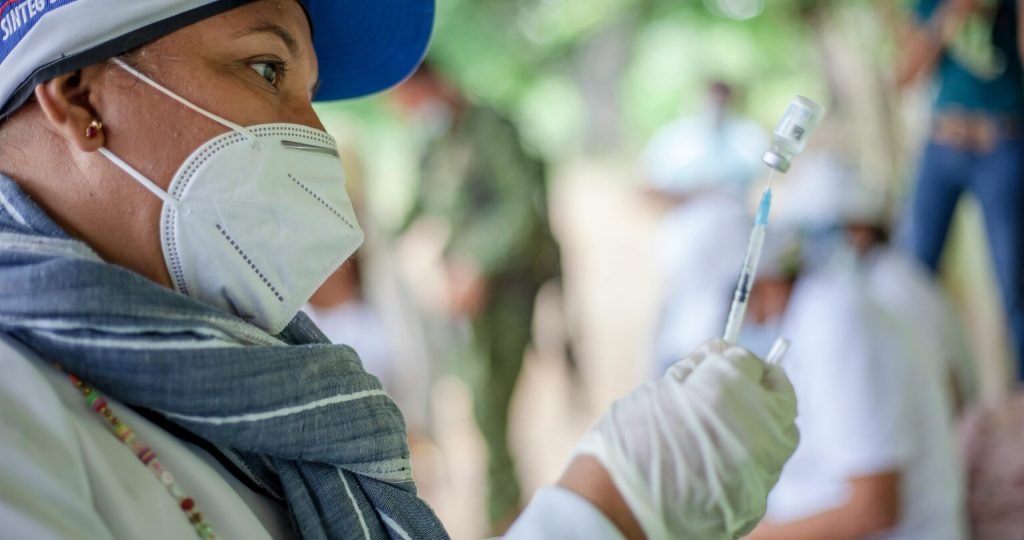 A healthcare worker prepares a vaccine outdoors in Ovejas, Colombia, emphasizing COVID-19 safety and healthcare provision.