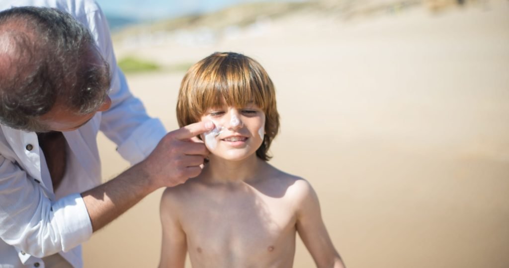 A father applying sunscreen to his son on a sunny Portuguese beach, emphasizing sun safety.