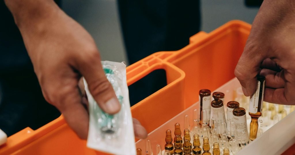 Close-up of hands organizing vials and syringe in a medical first aid kit, emphasizing emergency readiness.