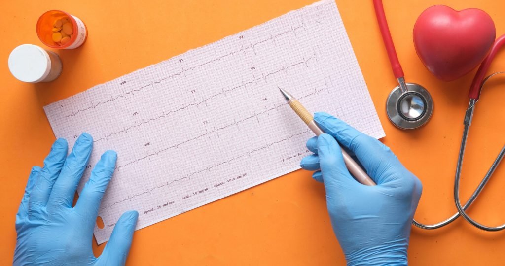 Hands with gloves analyzing an electrocardiogram on an orange background with stethoscope and pills.