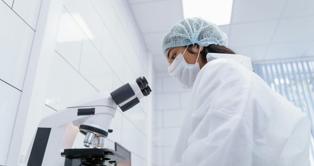 A scientist in protective gear uses a microscope in a modern laboratory setting.