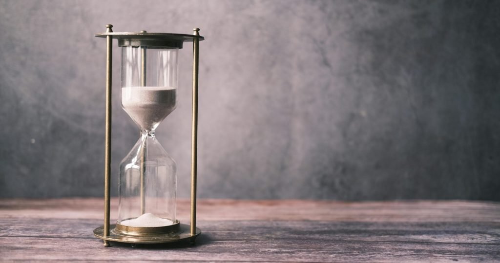 A classic hourglass with sand on a rustic wooden table against a soft gray background, offering ample copy space.